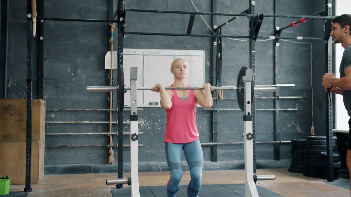 A member holding a front rack position at the squat stands while a coach watches from the next platform
