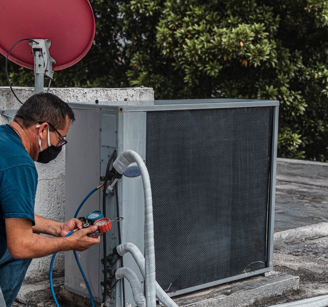 Technician checking a rooftop condenser with manifold gauges