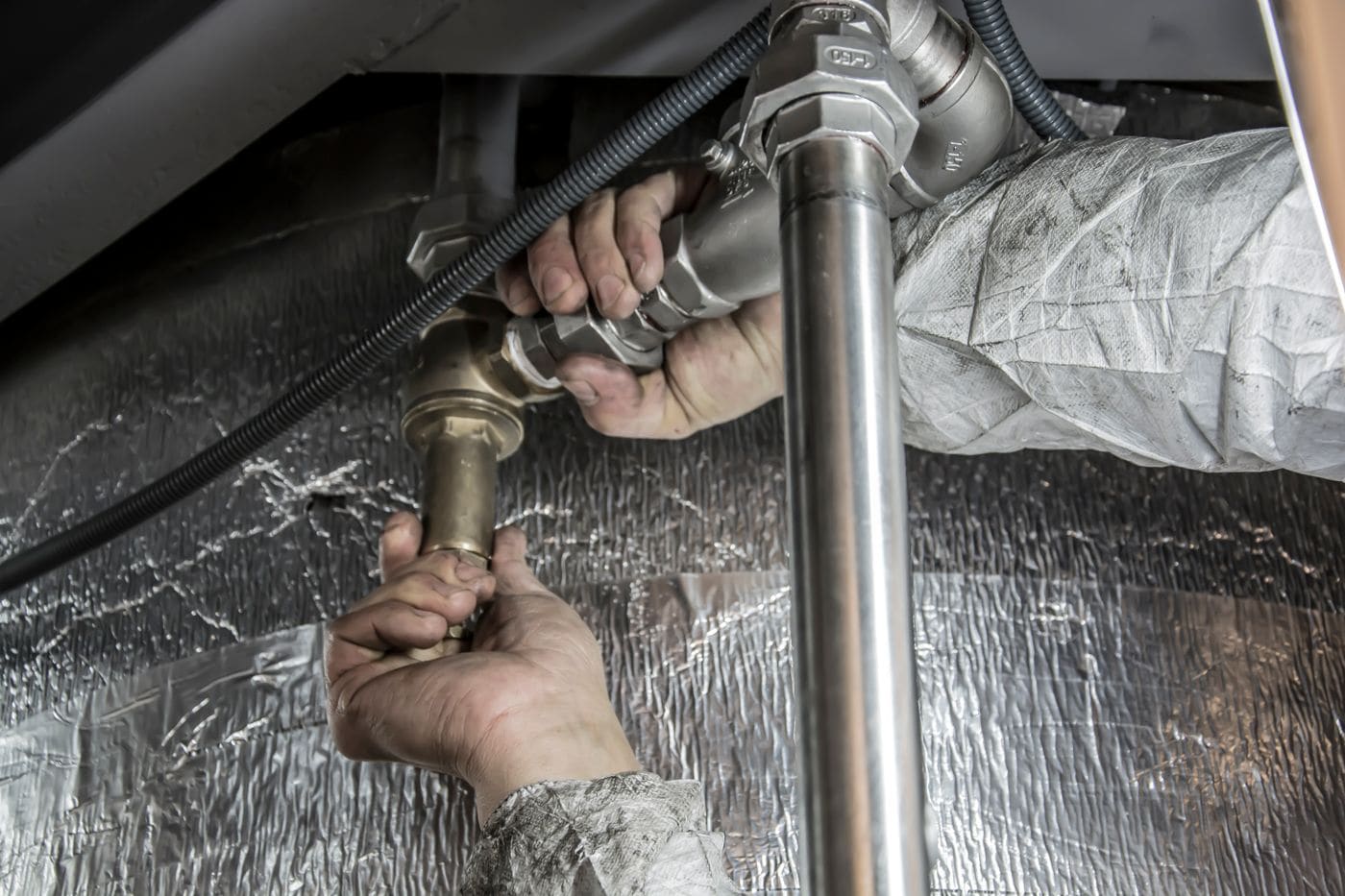Plumber tightening pipe fittings under a sink