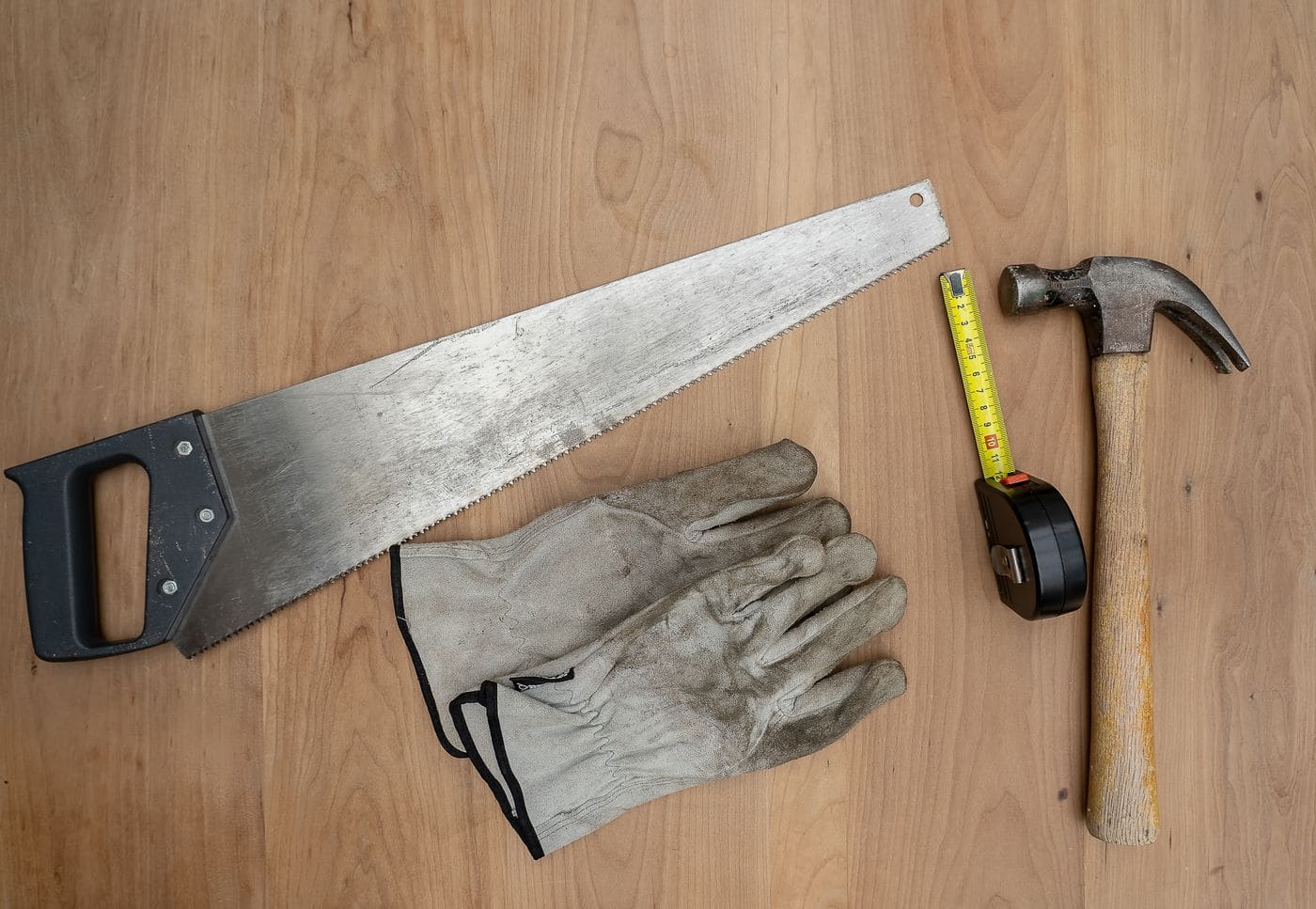 Hand saw, work gloves, tape measure and hammer laid out on a bench