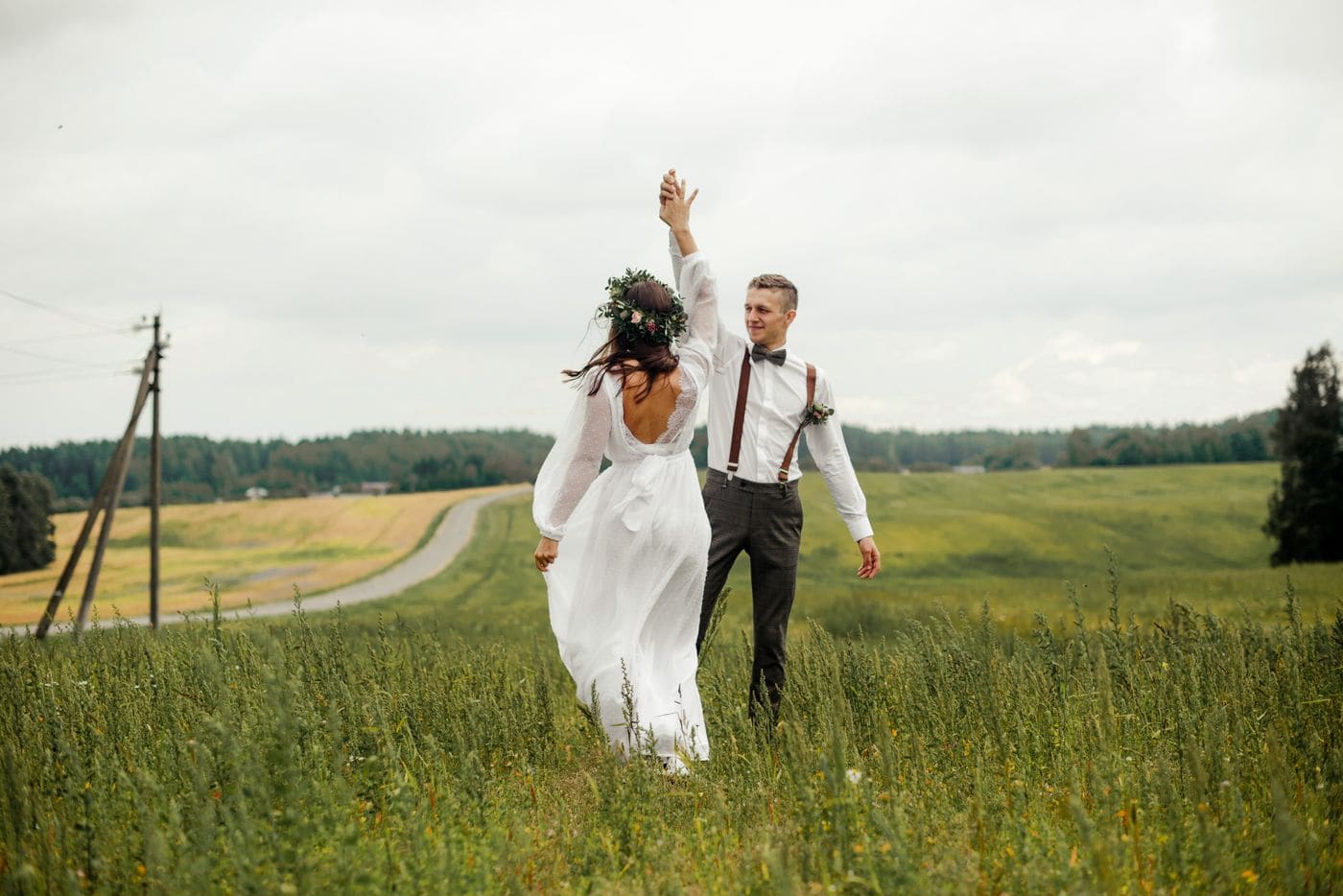 A couple walking through long grass on a headland under a low overcast sky, a road behind them